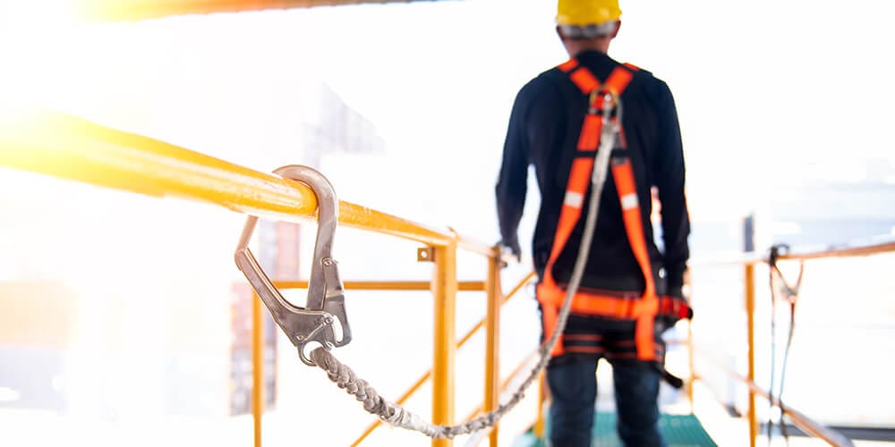 Dělník ve výšce s úvazkem a ochranným postrojem připravený k vyklízecím pracím.